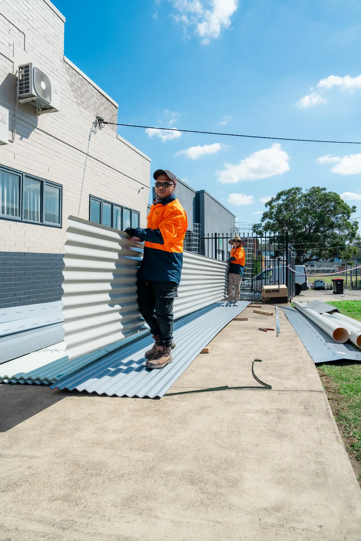 Roofer standing new corrugated metal sheets upright beside an industrial building