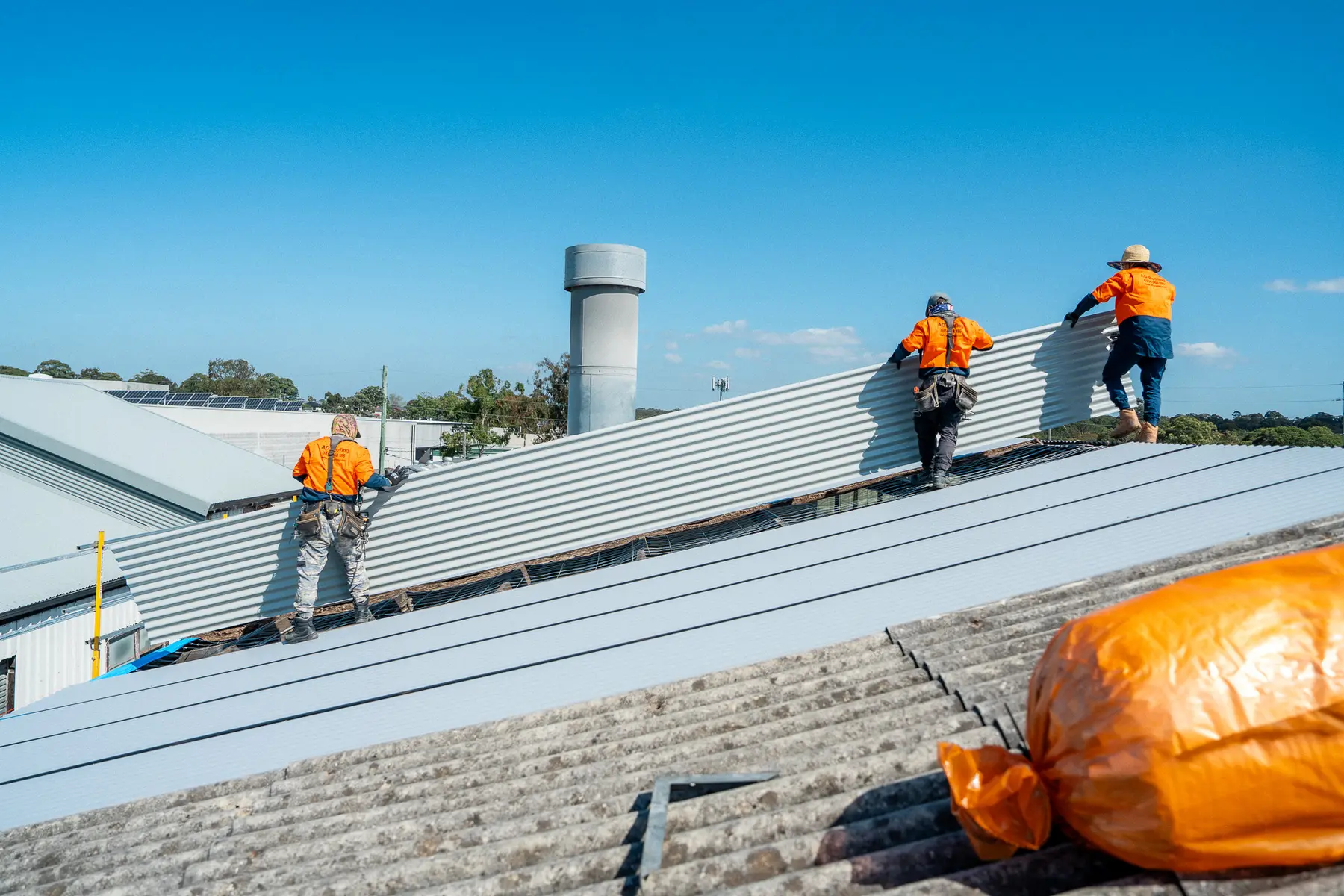 AD Roofing crew carrying a long sheet across an industrial roof during a re-roof