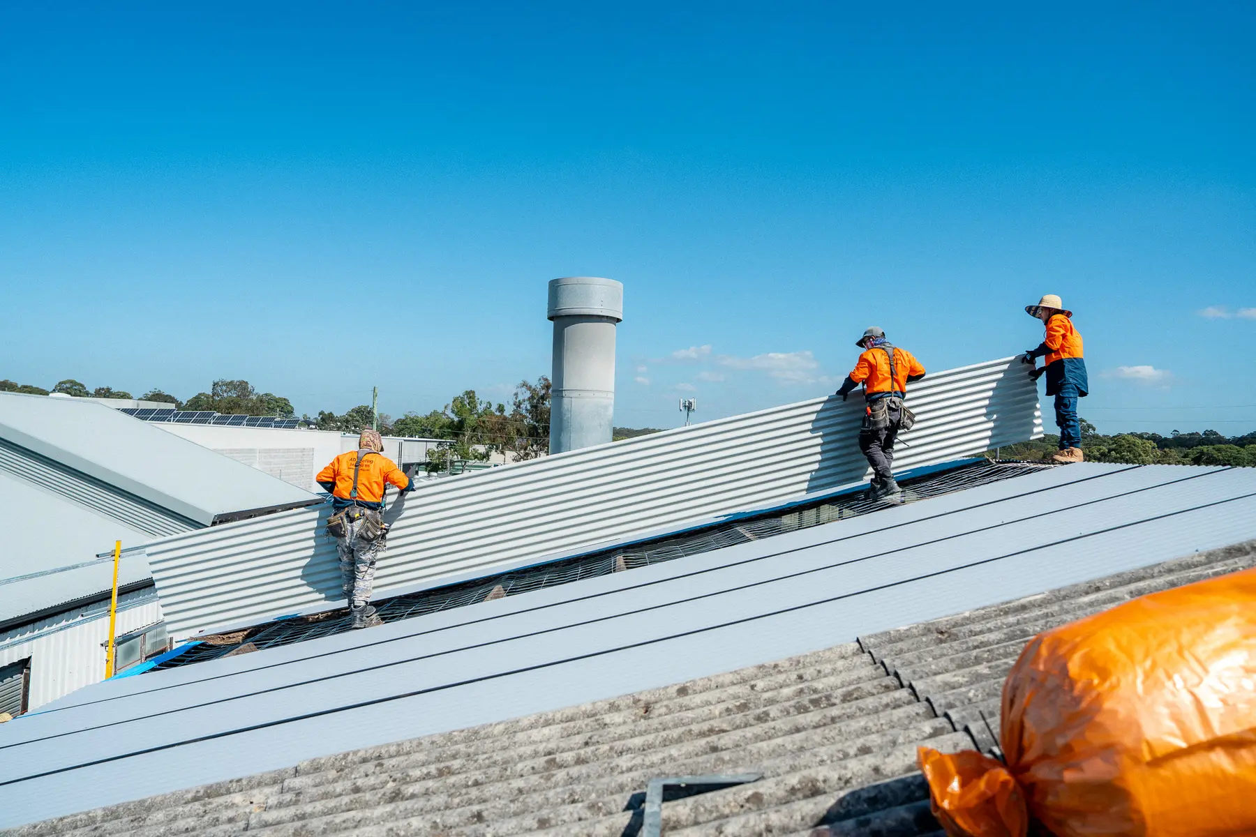 Roofers walking a new roof sheet into place on a large industrial roof