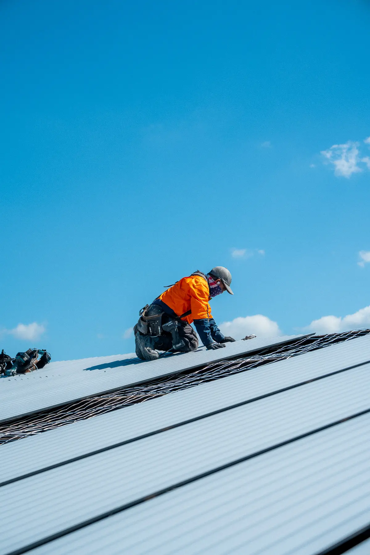 Roofer kneeling to fix a new sheet on an industrial roof