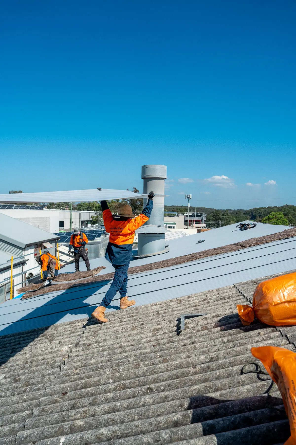 Roofer carrying a new metal sheet over an old corrugated fibre-cement roof