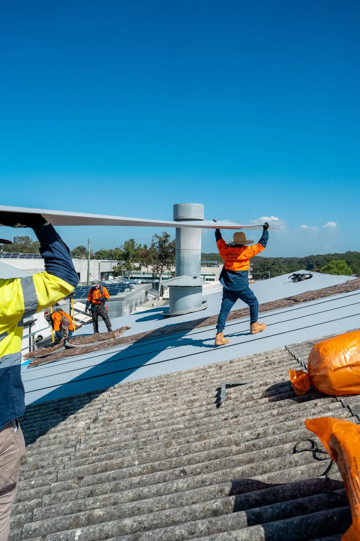 Two roofers carrying a new roof sheet across an industrial roof