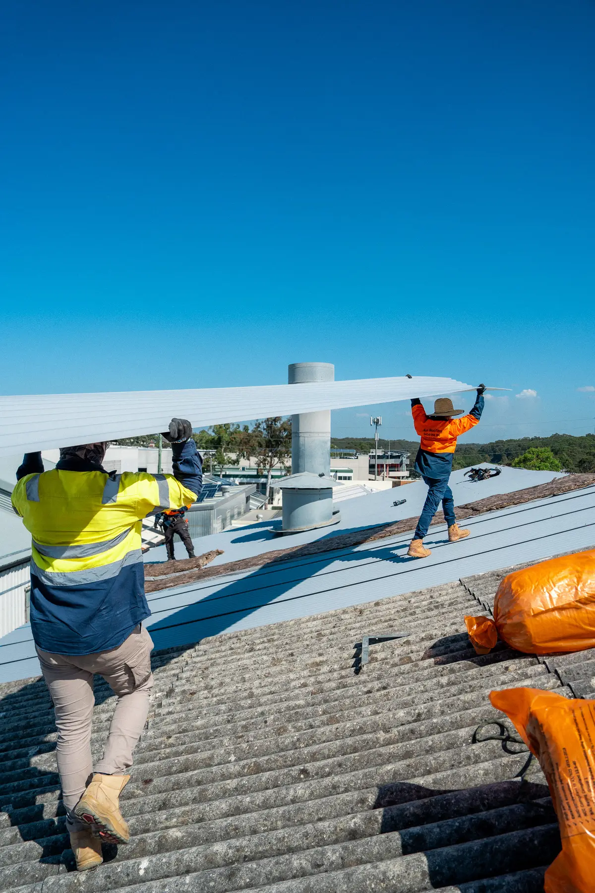 Crew walking a long sheet across the old corrugated roof