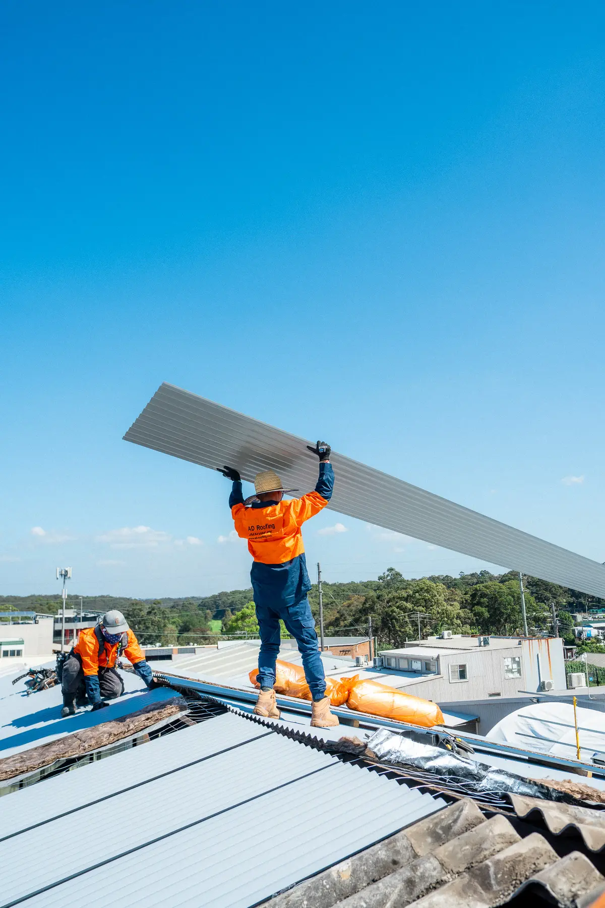 AD Roofing roofer holding a long new metal roof sheet overhead