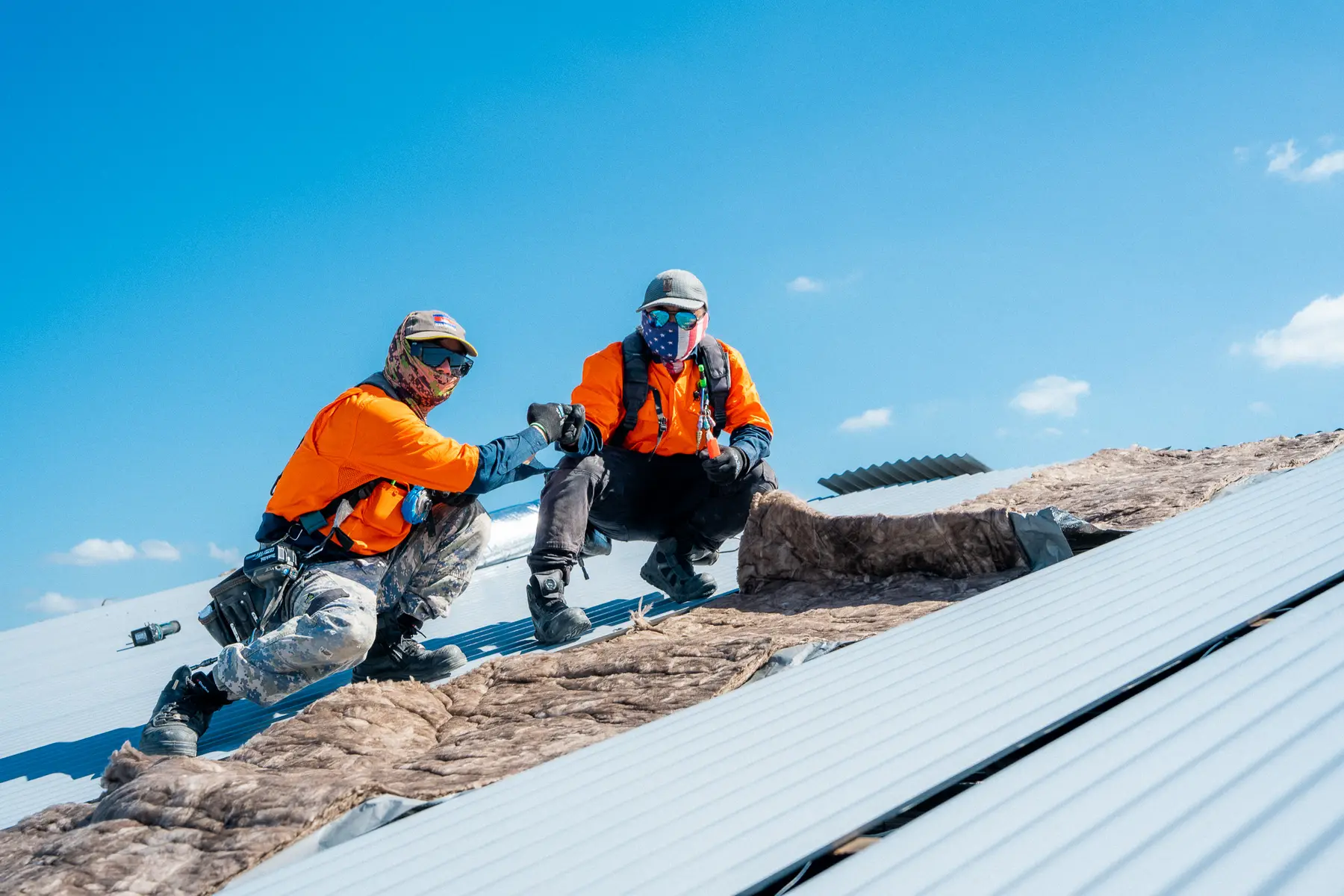 Two AD Roofing roofers crouched on new roof sheets during an industrial re-roof