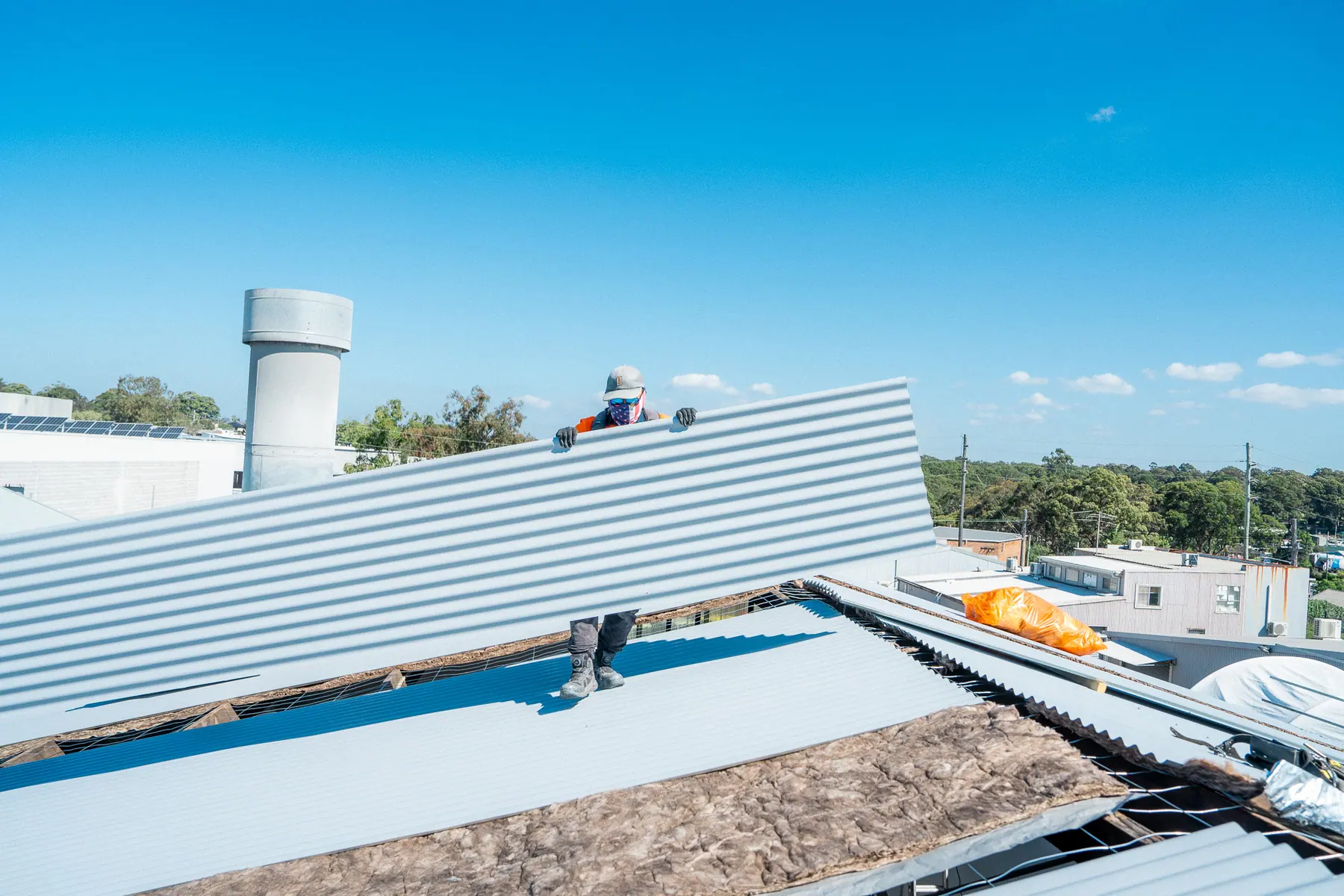 New metal roof sheet being slid into place beside a roof ventilator