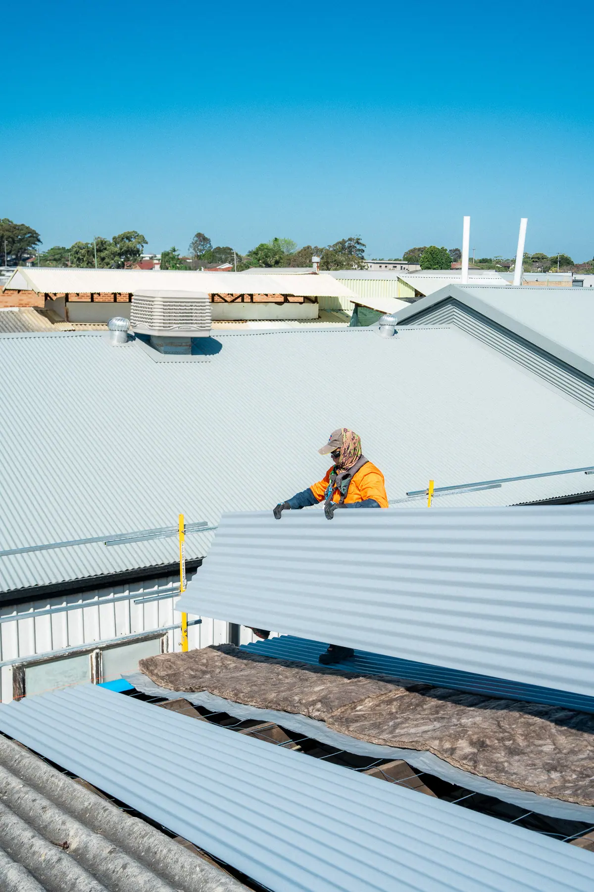Roofer kneeling to fix new metal sheets on a commercial roof