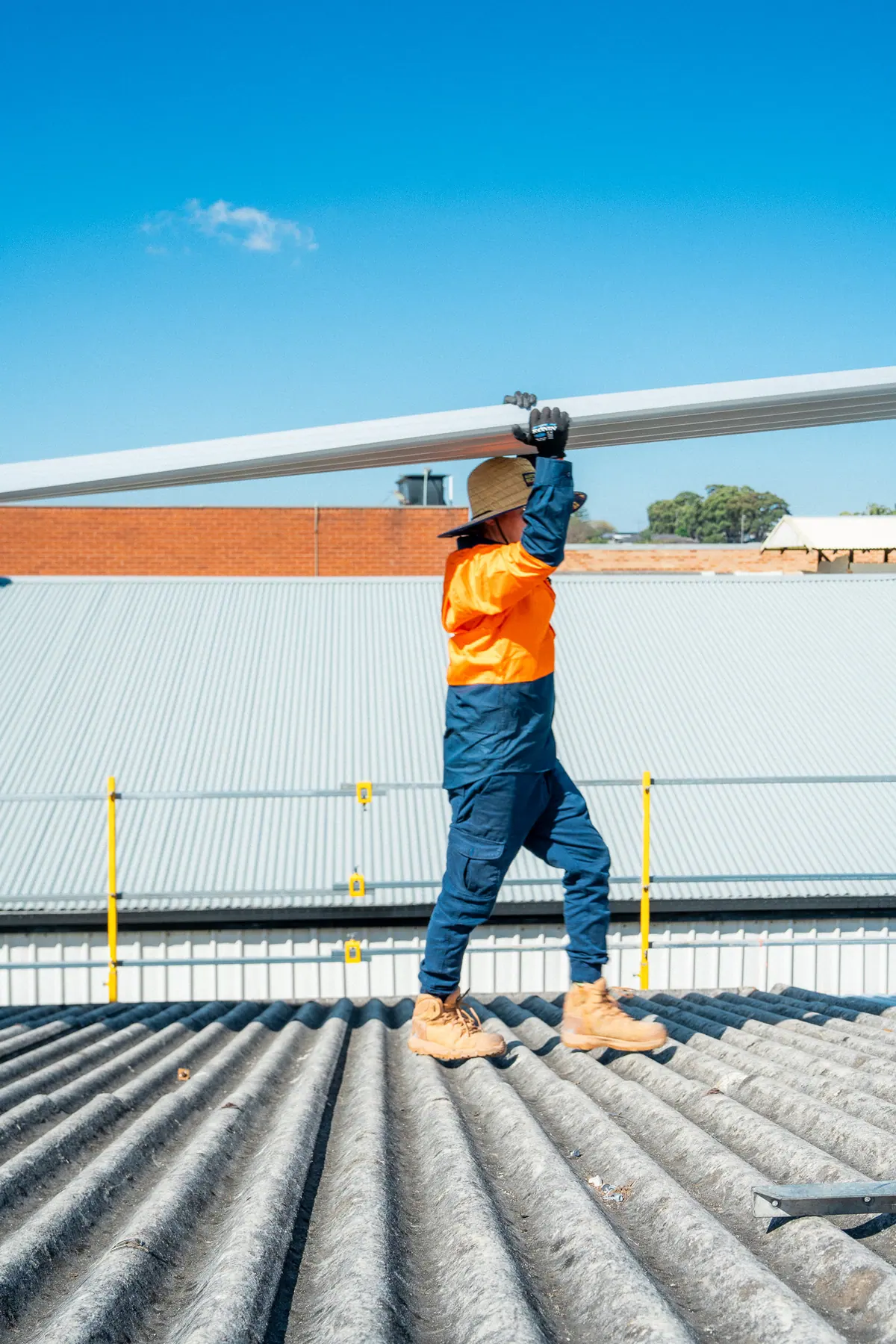 Roofer carrying a long metal roof sheet overhead across the roof