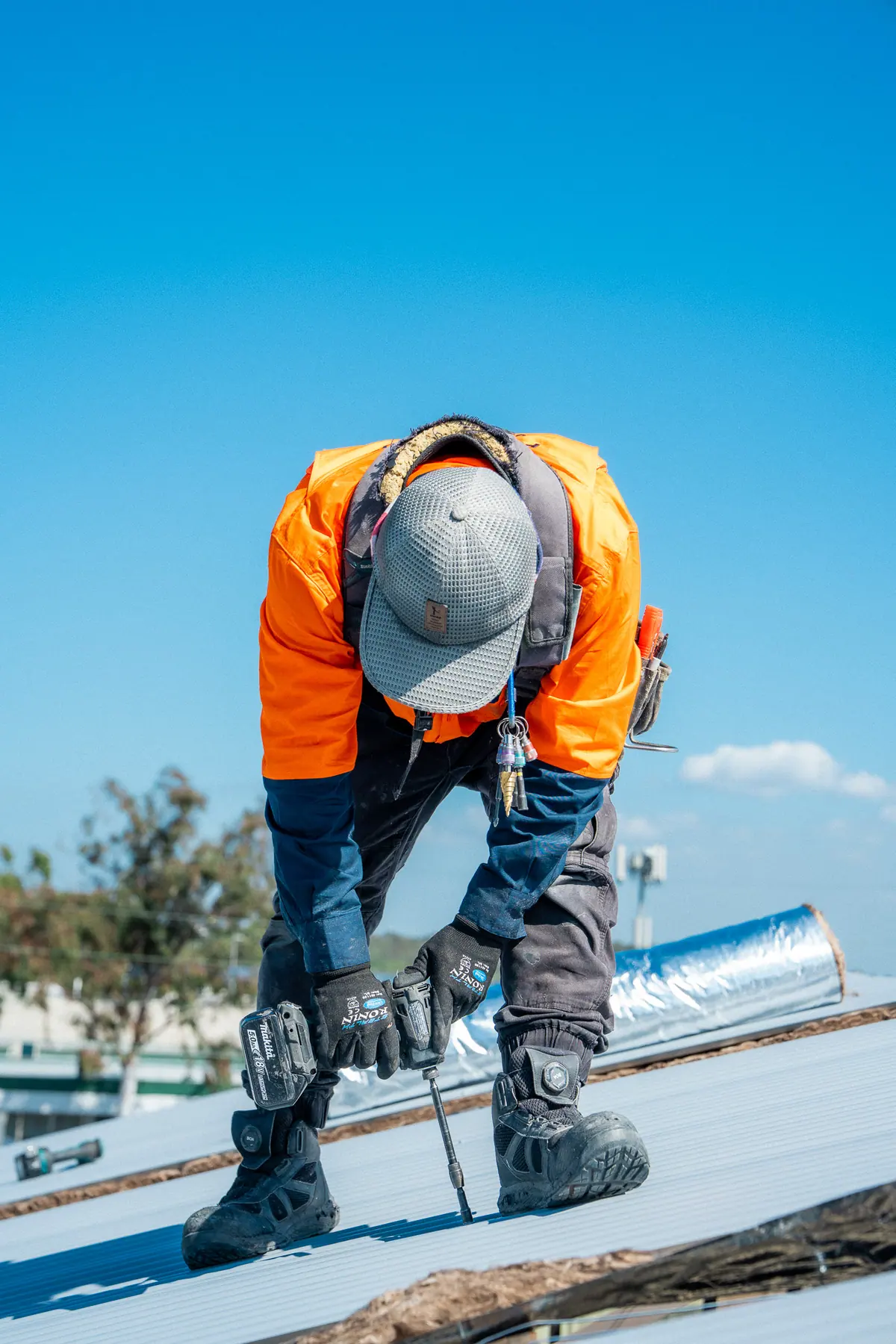 Roofer in a hard hat drilling roofing screws into new metal sheets