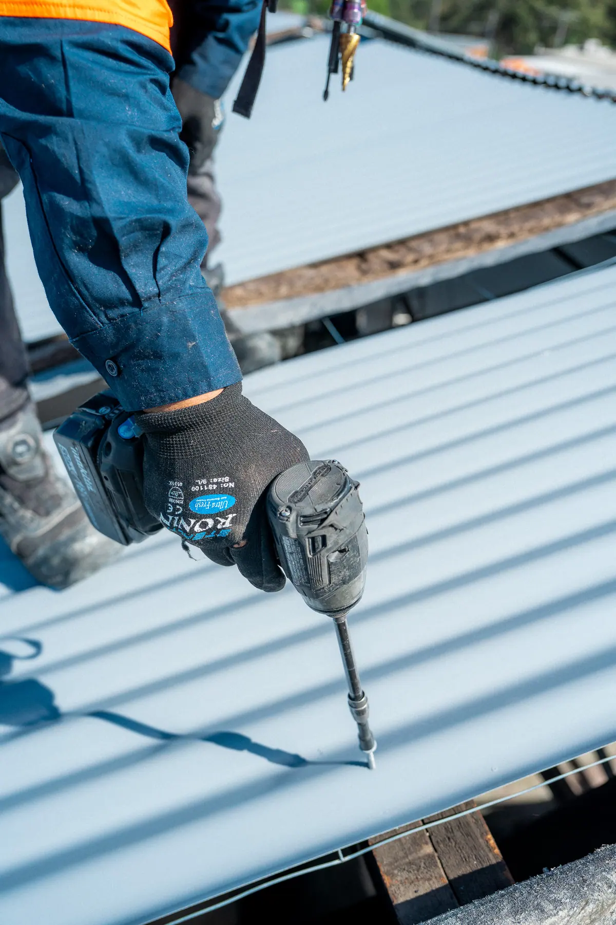 Close-up of a cordless drill driving a roofing screw into new sheeting