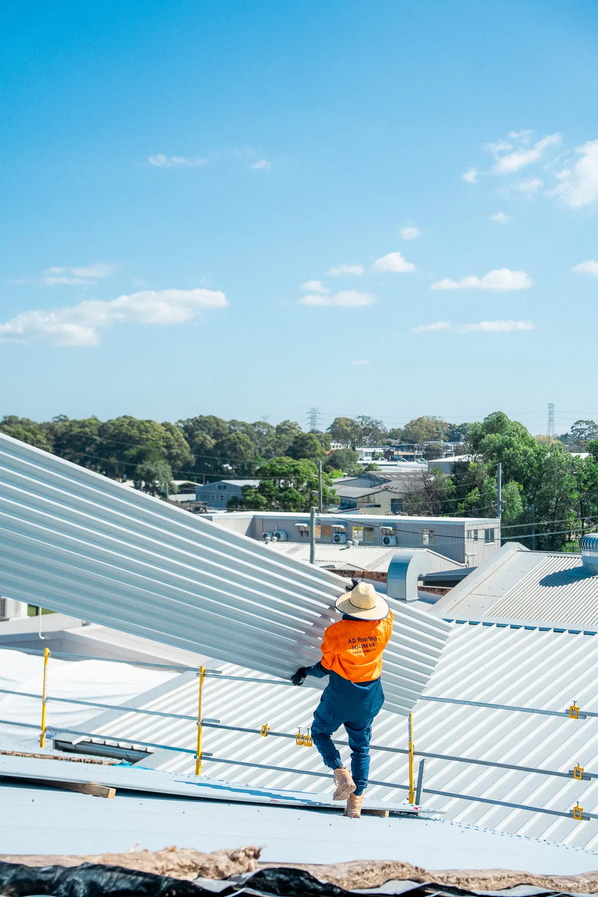 Roofer carrying a new roof sheet along the roof with surrounding rooftops behind