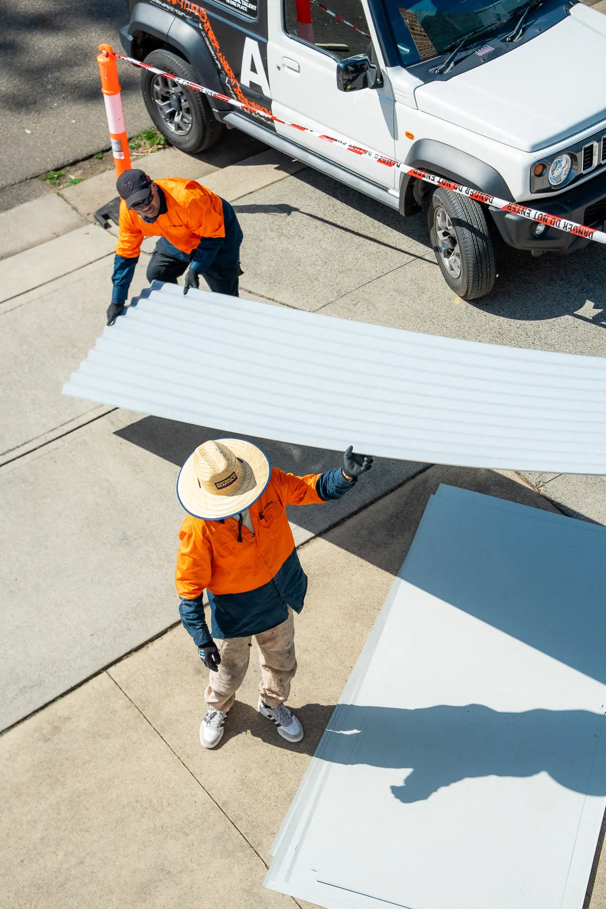 Crew passing a metal roof sheet up from the ground beside the work vehicle