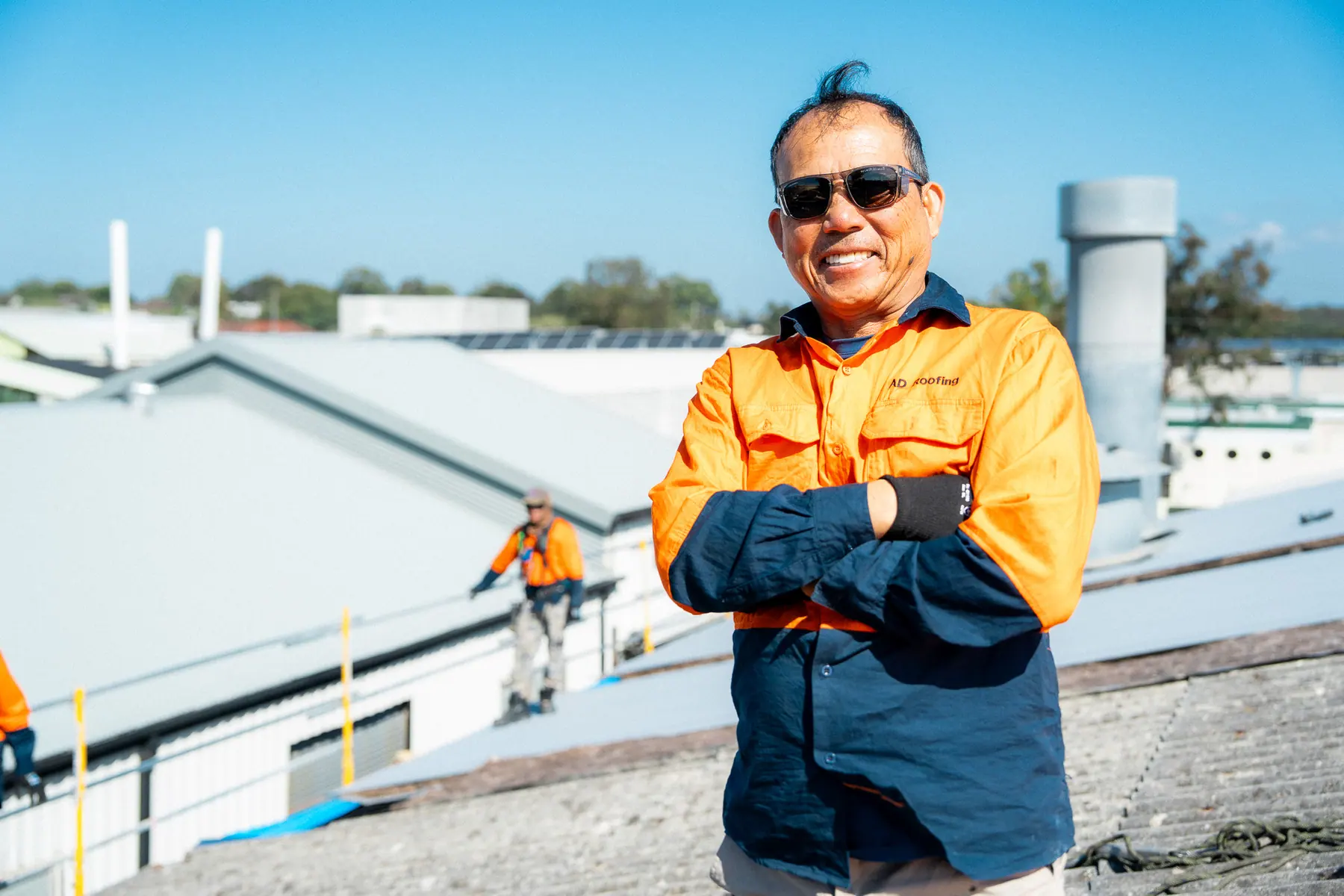 AD Roofing roofer standing with arms crossed on the roof while the crew works behind