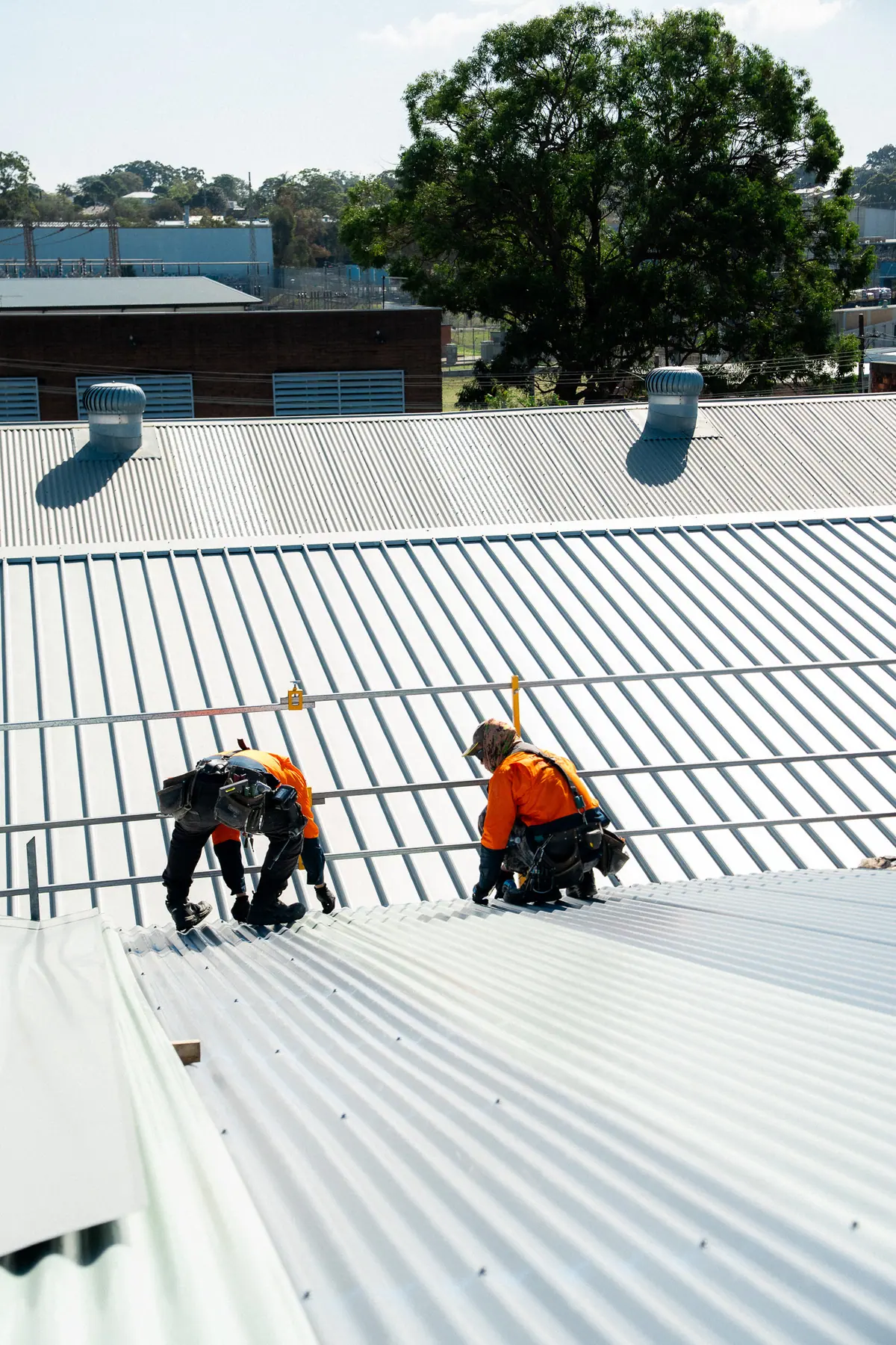 Two roofers fixing new sheets on a wide commercial roof