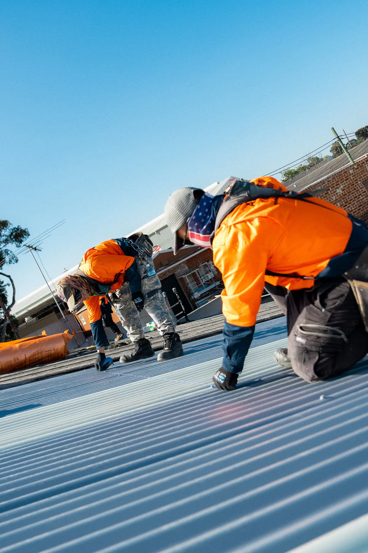Roofer kneeling to drive screws along a new sheet