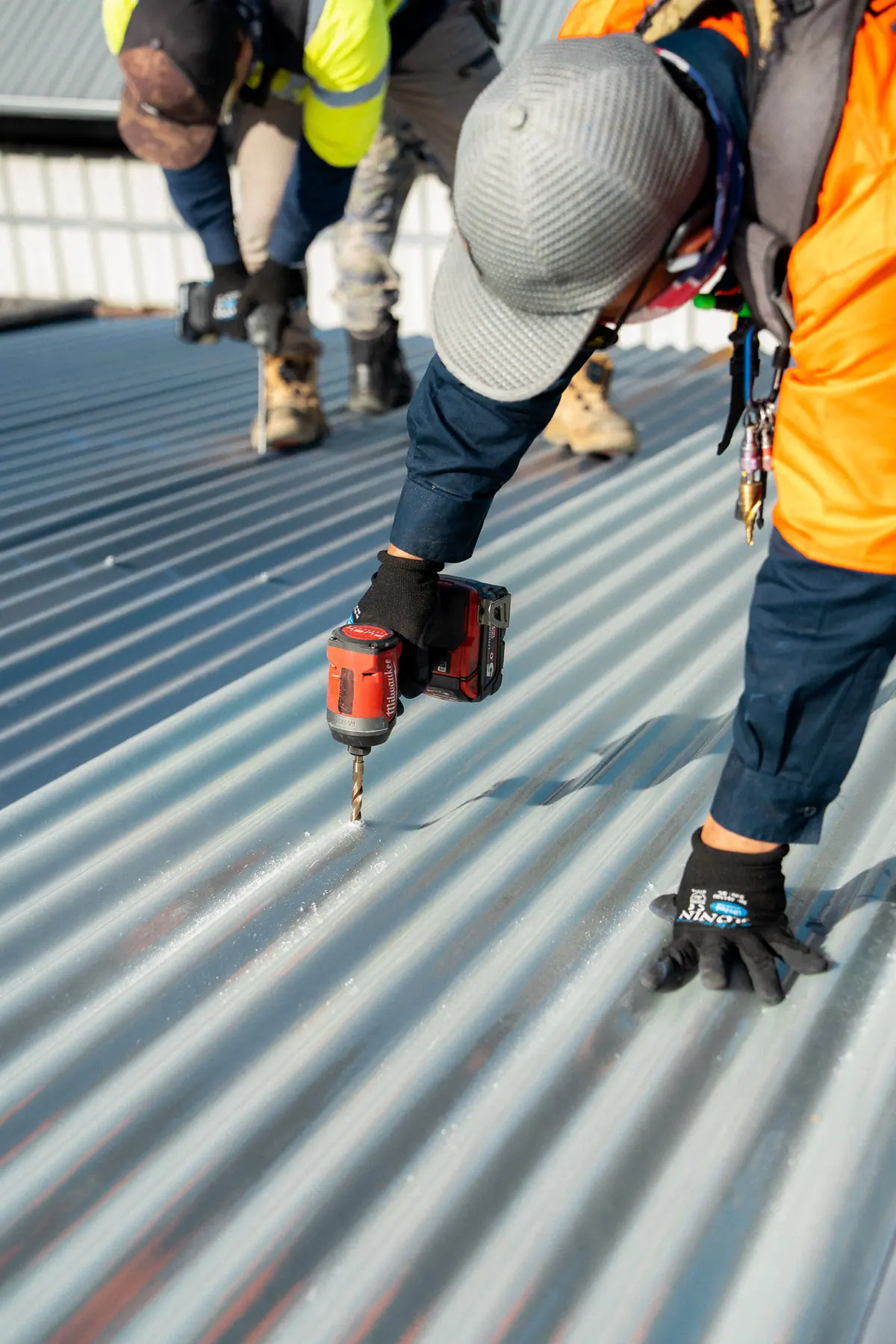 Close-up of a roofer driving screws into new metal roof sheeting