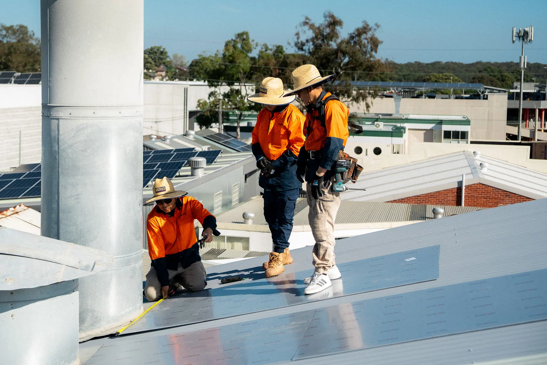 Roofers in wide-brim hats working beside a tall roof ventilator