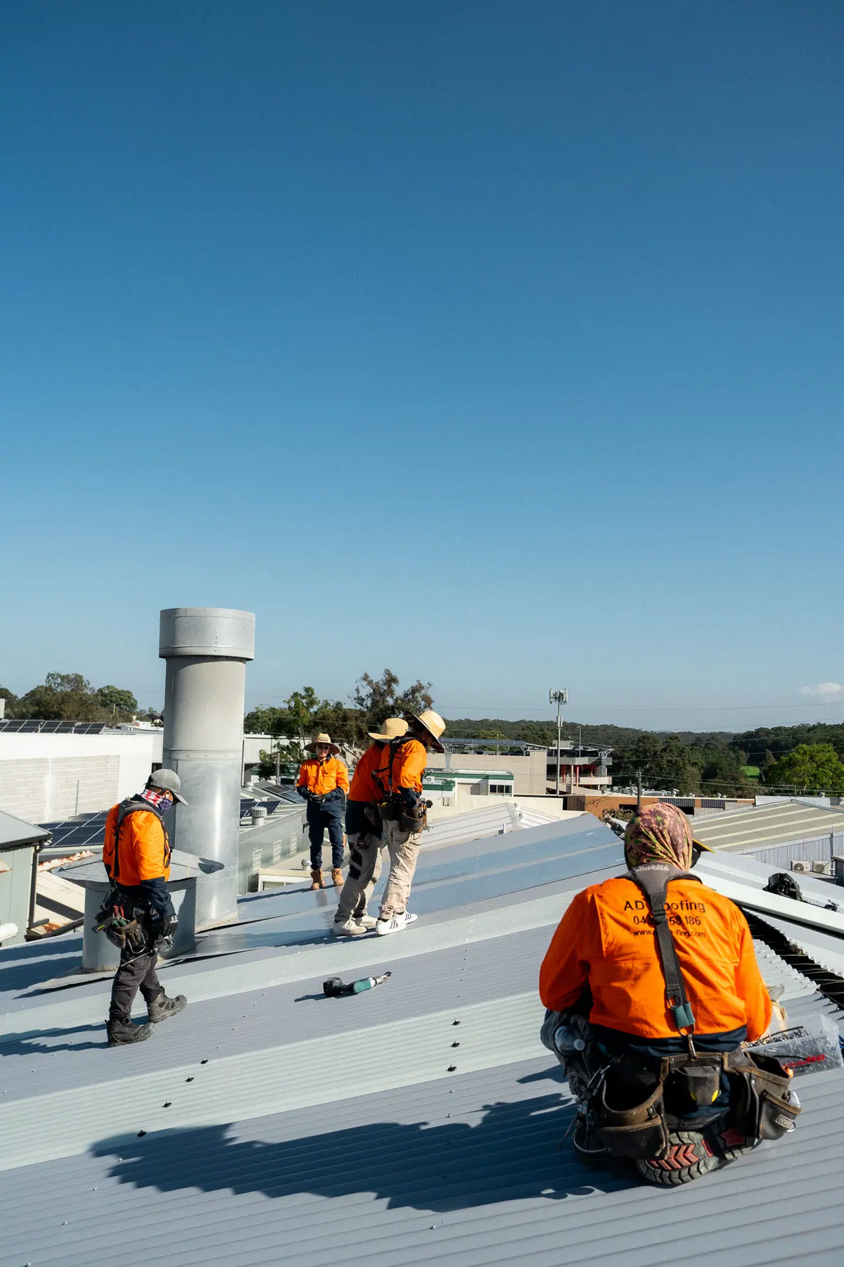 Roofer kneeling on the new roof as the crew works behind