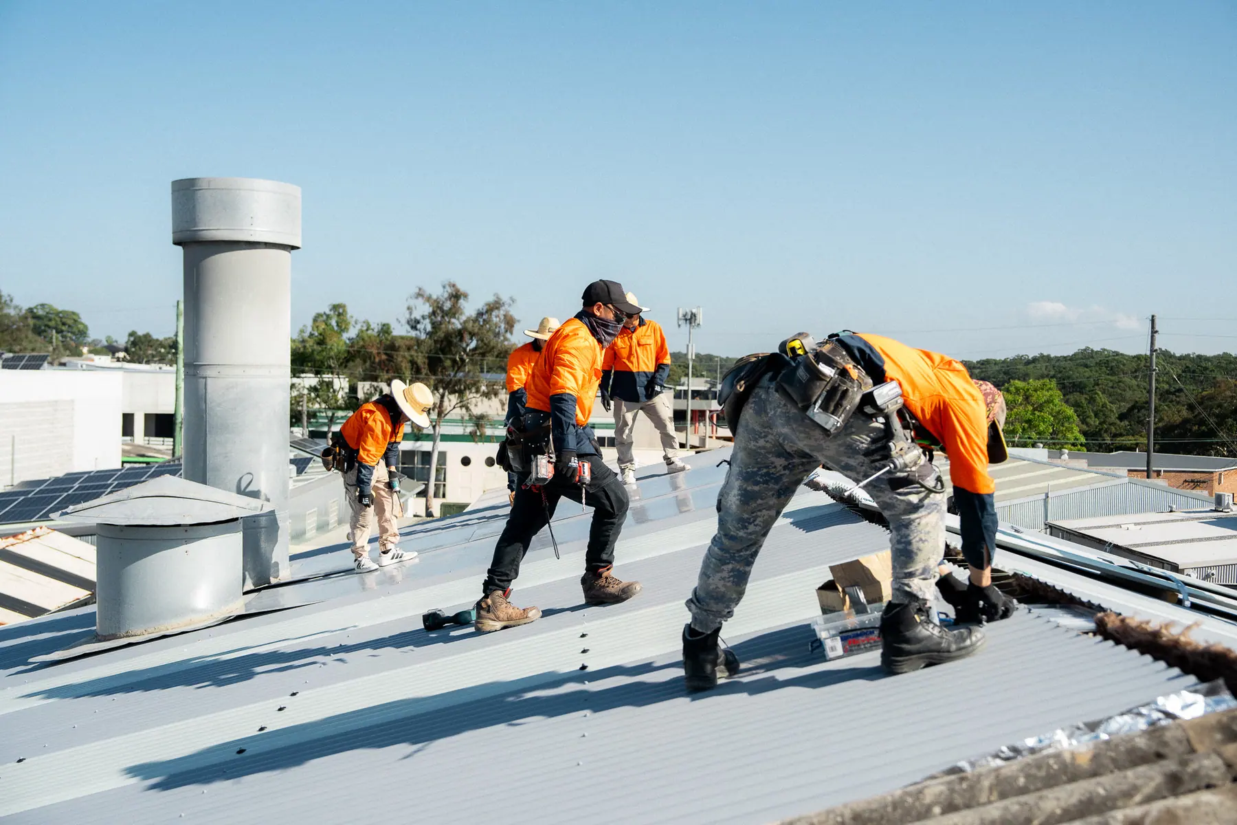 Roofer kneeling to fix sheets beside a roof ventilator