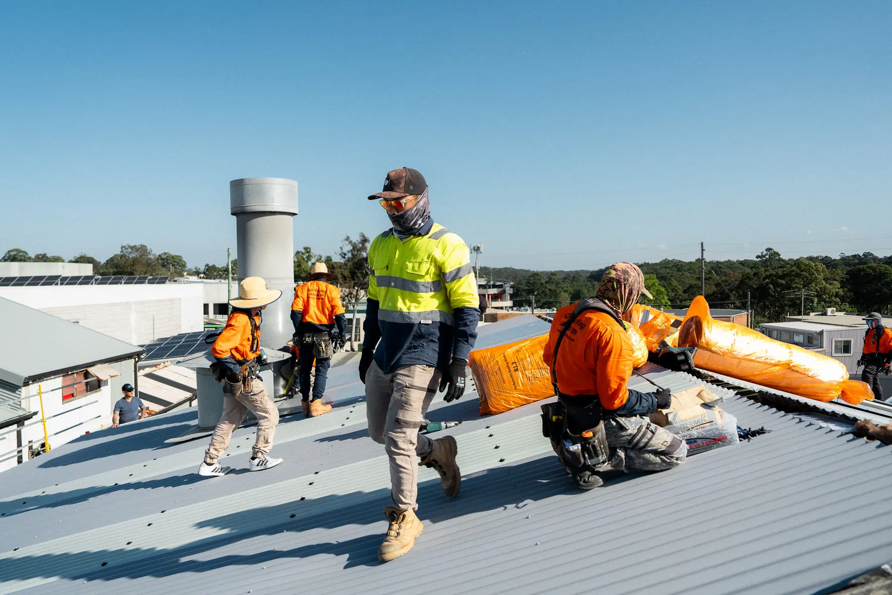 Crew rolling out orange-wrapped insulation blanket across the roof
