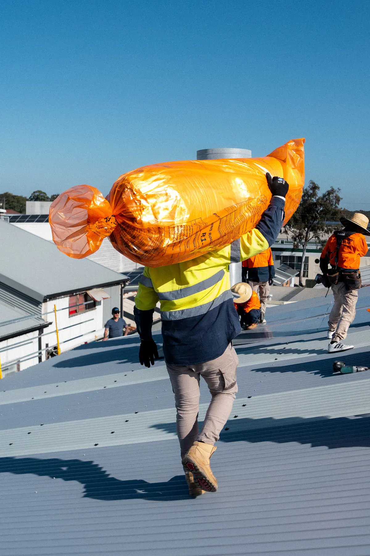 Roofer carrying a roll of insulation blanket on their shoulder